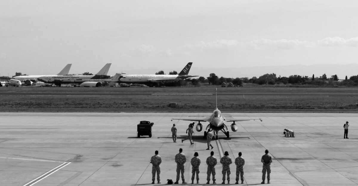 Black and white image of military personnel and jet at Istanbul airfield with parked aircraft in the background