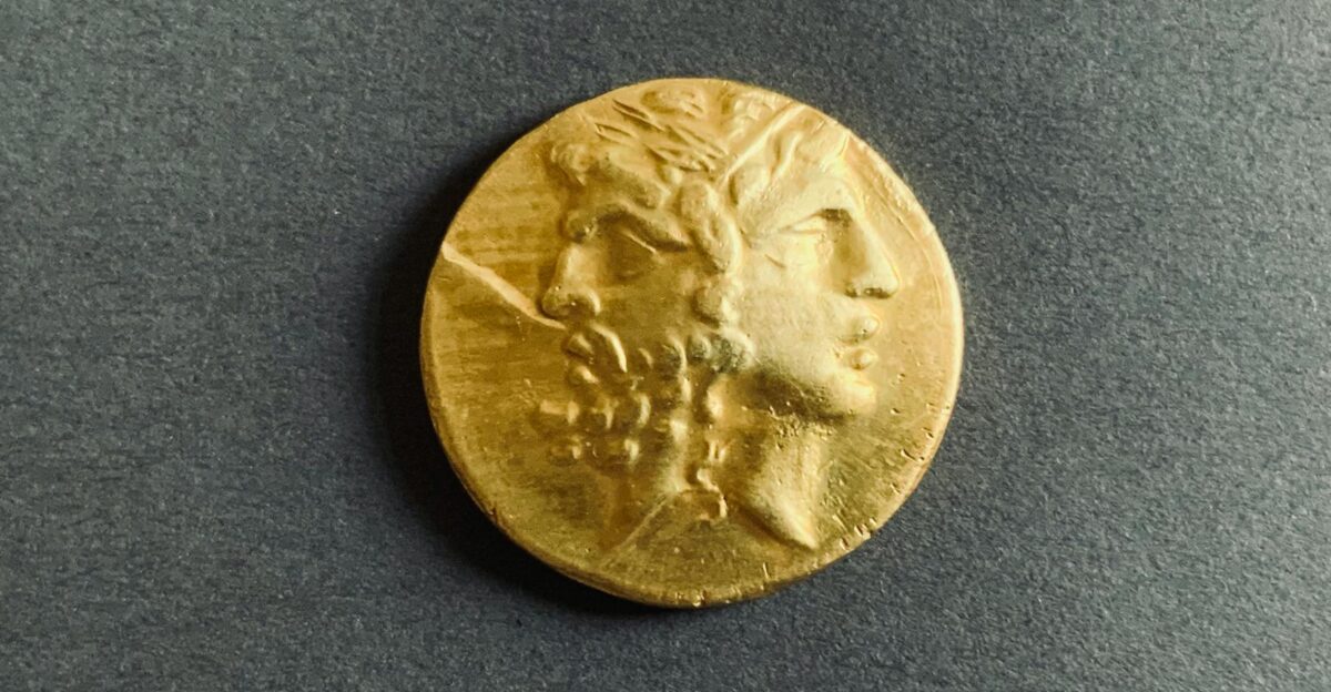 Close-up of an ancient golden coin with two faces on a dark background