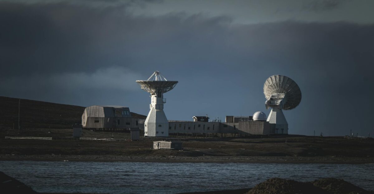 A remote satellite station with large dishes stands under a moody dark sky by the water