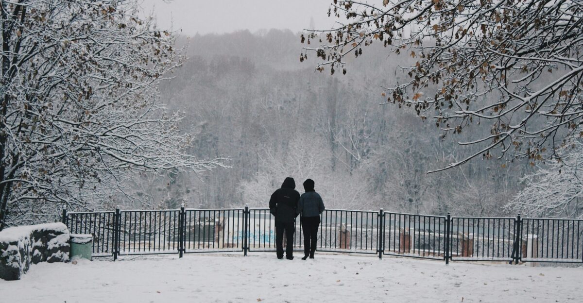 two people standing in the snow near a fence