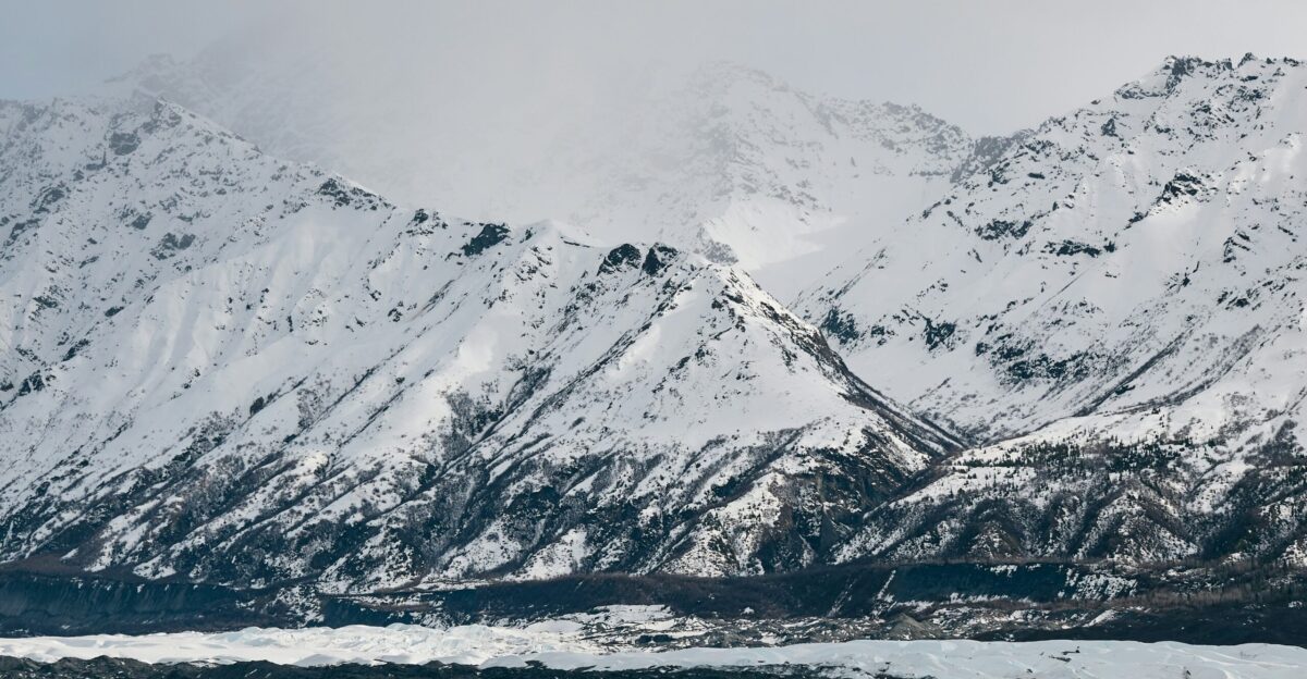 Snow-covered mountains loom under a cloudy sky