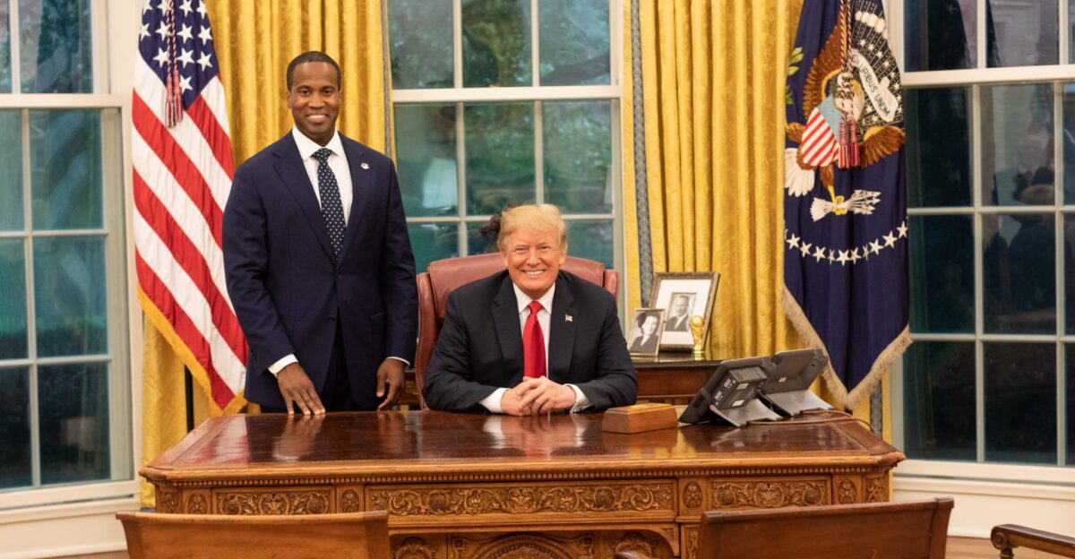 President Donald Trump seated behind the Resolute desk with 2018 Michigan senatorial candidate John James in the Oval Office