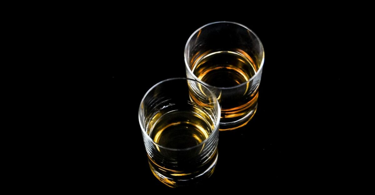Two whiskey glasses with amber liquid reflecting on a glossy black surface