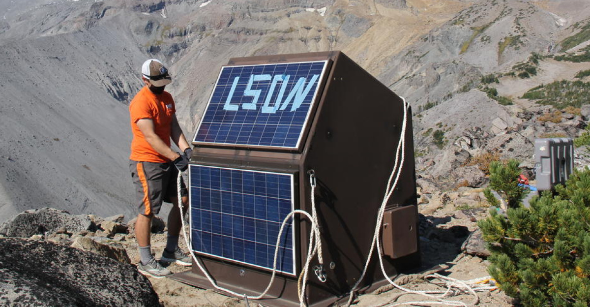 USGS Cascades Volcano Observatory Geophysicist Wes Thelen, removes ropes from new station LSON, at Mount Hood (Mount Hood is pictured in the distance). The fiberglass hut, delivered by helicopter, will house a power supply, data digitizer and other equipment necessary to collect and send seismic and GPS data to the Cascades Volcano Observatory and their monitoring partners.