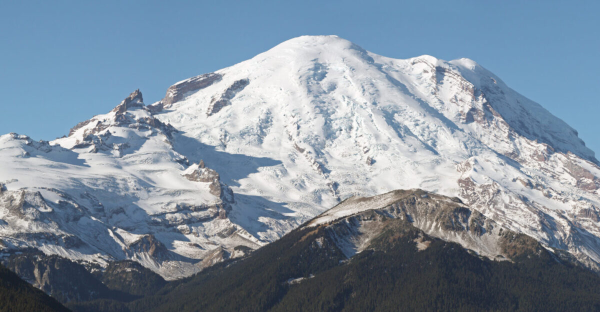 Mount Rainier with its main summit Columbia Crest 14410 feet at the center Emmons Glacier covers most of the visible flank of the mountain Ingraham Glacier left is between Gibraltar Rock 12660 feet high on the left skyline and Disappointment Cleaver Left of Gibraltar Rock is sharp pointed Little Tahoma 11138 feet with Frying Pan Glacier on its flank It is the source of Frying Pan Creek not visible in the valley left of forested and rounded Goat Island Mountain in front of the Emmons Glacier Liberty Cap 14112 feet is visible on the right center skyline behind Russell Cliff Curtis Ridge descends to the right from Russell Cliff Winthrop Glacier flows right below Curtis Ridge and behind shallow Steamboat Prow 9680 feet with the small Inter Glacier on its northeast face The White River not visible comes from the Emmons Glacier and flows around the right side of Goat Island Mountain