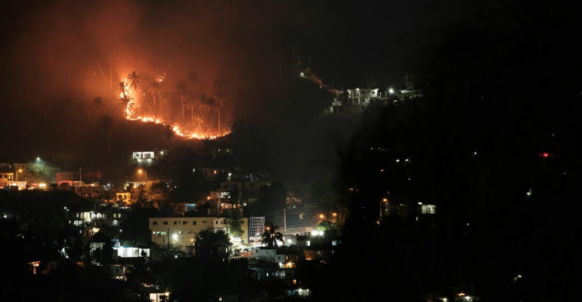 Aerial view of a forest fire at night near a town with bright flames lighting up the sky and smoke billowing upwards