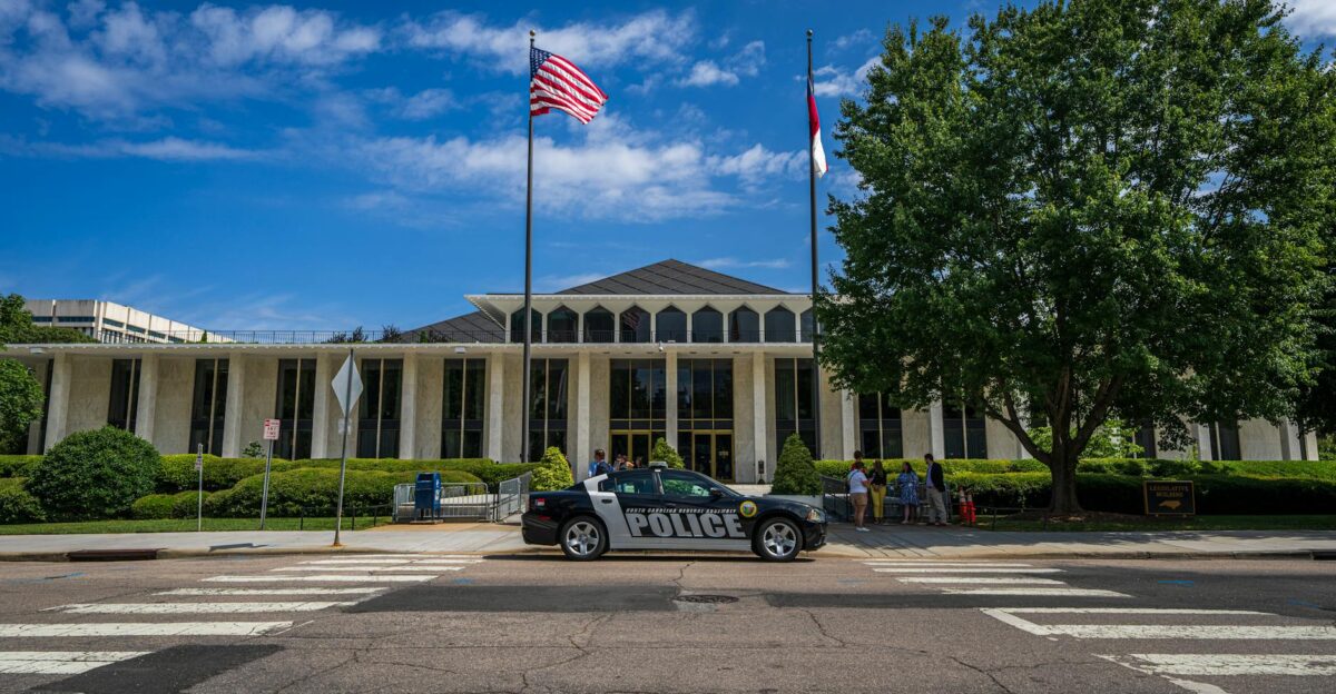 Government building facade with flags and police car in front on a sunny day