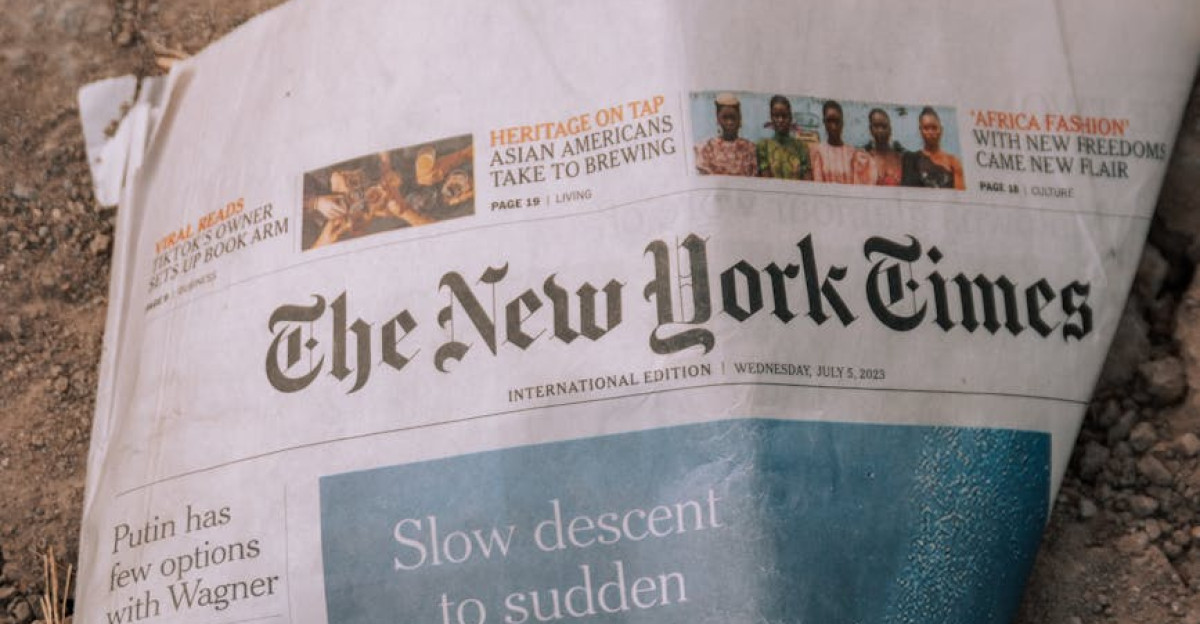 A wrinkled The New York Times newspaper lies on a dirt surface outdoors