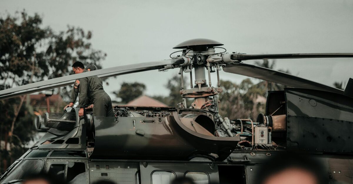 A military helicopter with crew performing maintenance during daytime outdoors