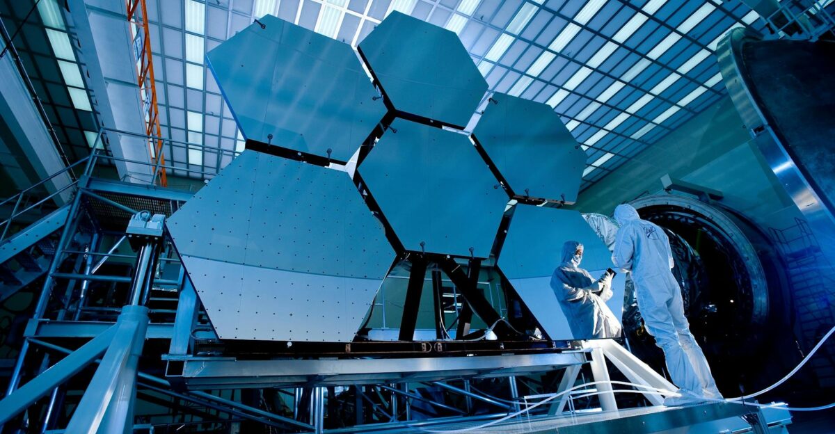 Engineers in protective suits work on telescopic mirrors in a high-tech lab