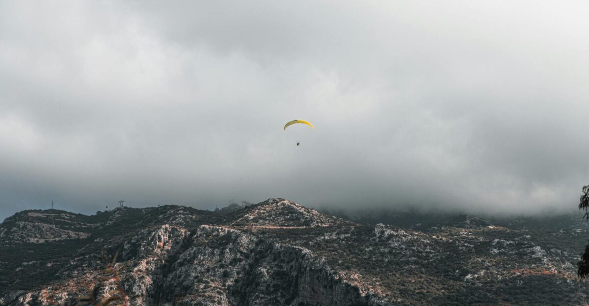 A paraglider gracefully flies over rugged mountainous terrain beneath a cloudy sky showcasing adventure