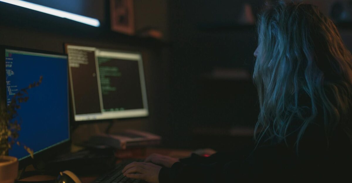 A woman working on programming tasks with multiple screens in a dimly lit room