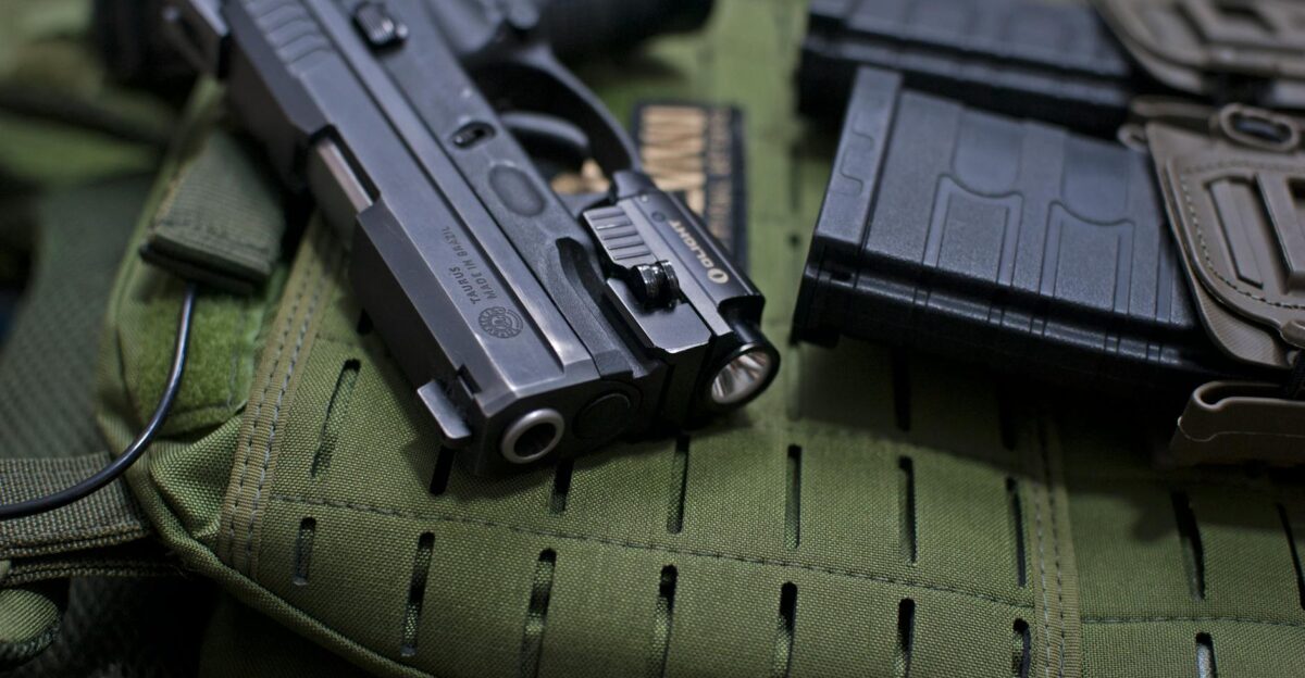 Handgun placed on military gear with tactical accessories emphasizing modern defense tools