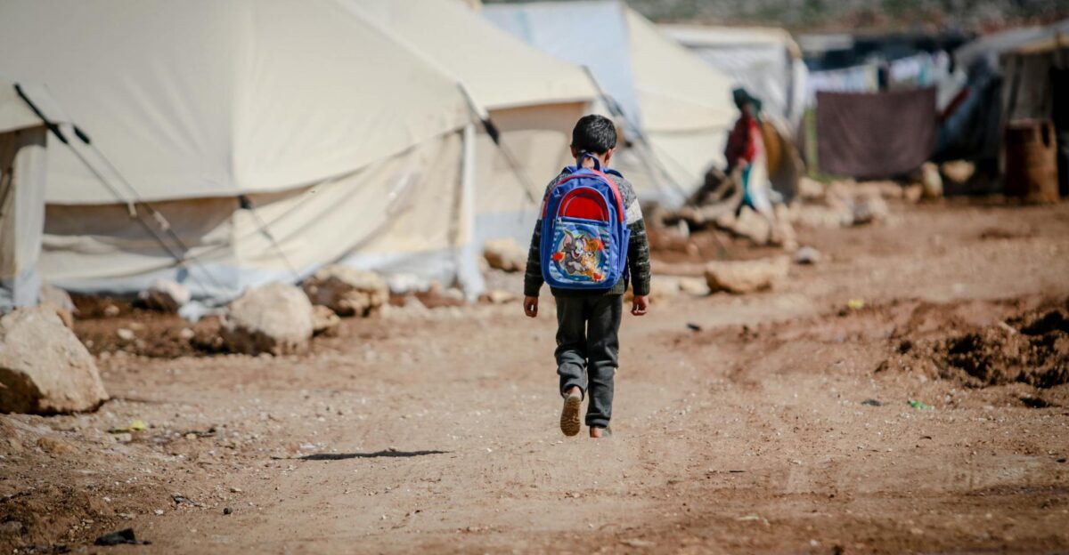 A young boy carrying a backpack walks in a refugee camp in Idlib Syria