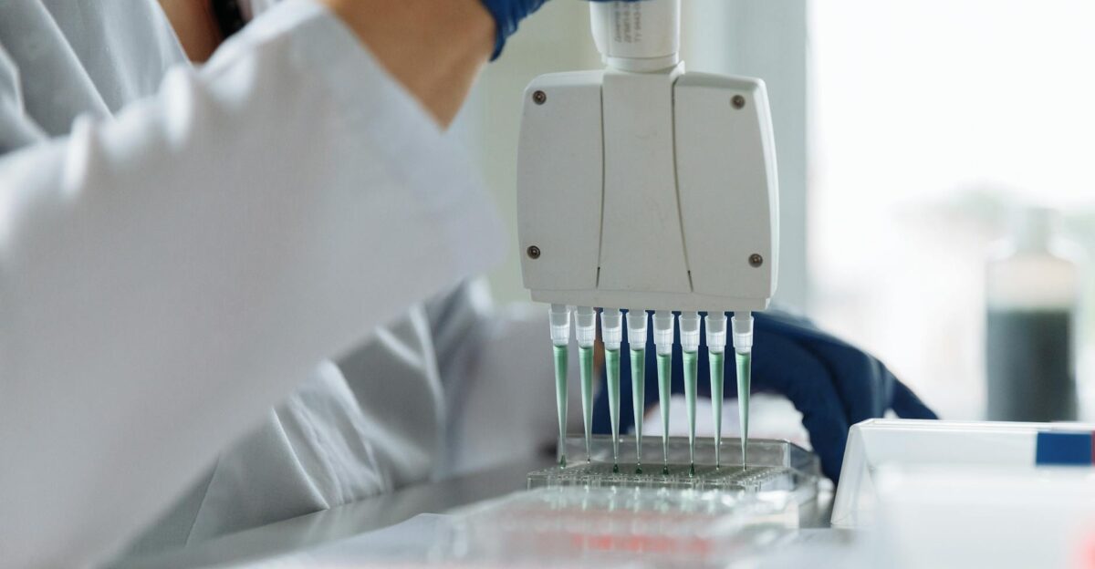 A scientist wearing a lab coat uses a multichannel pipette for liquid handling in a lab setting