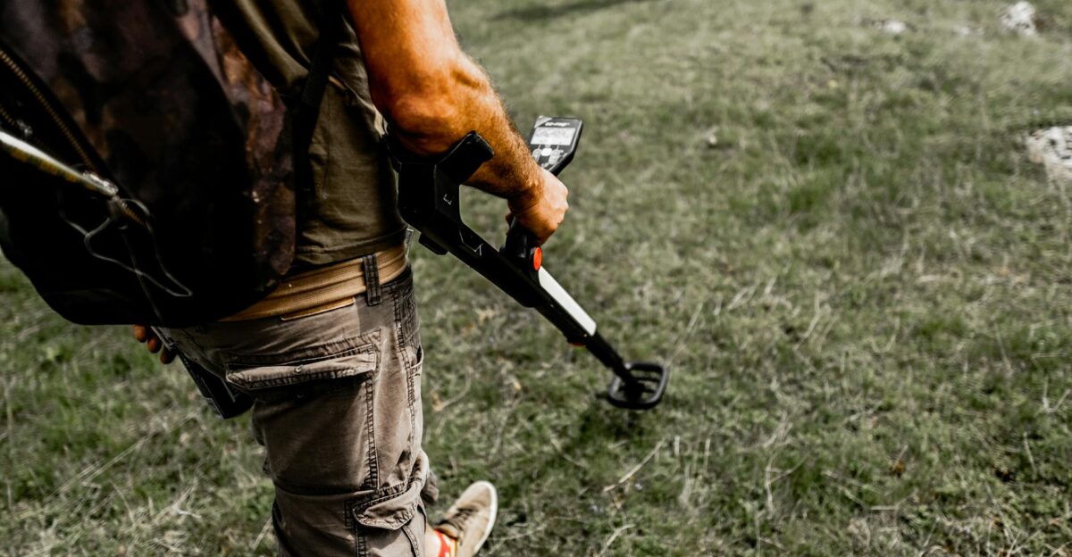 Person using a metal detector on a grassy field wearing casual attire