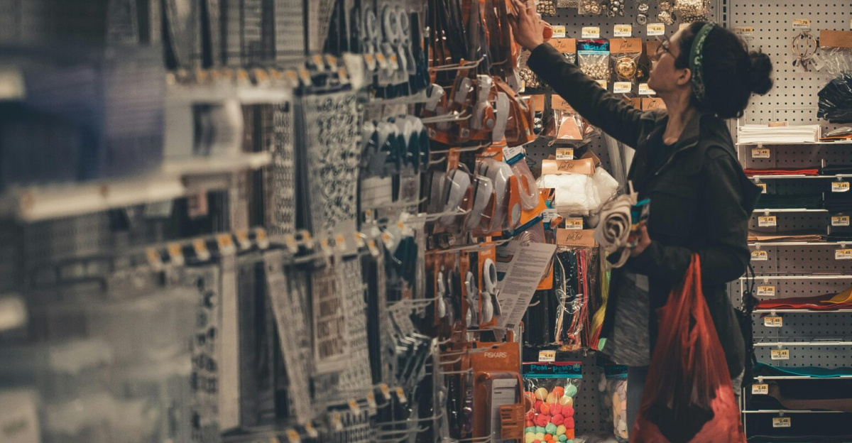 Woman reaching for items in a busy craft store aisle, exploring various art supplies.
