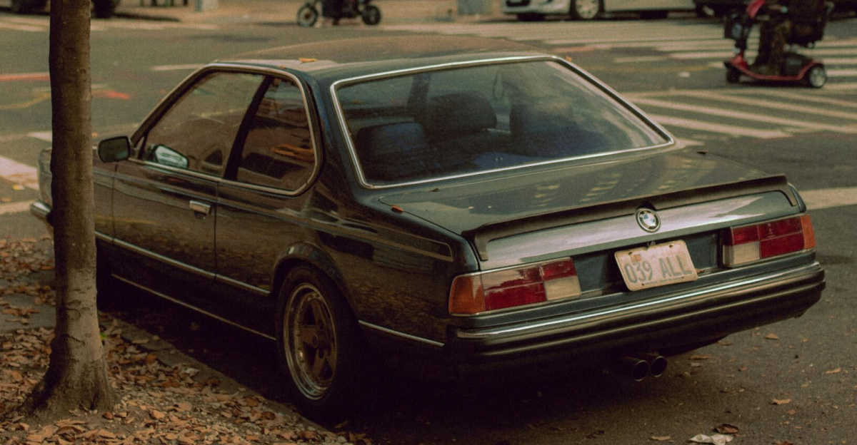 A parked BMW on a city street in autumn, surrounded by urban life and fall foliage.