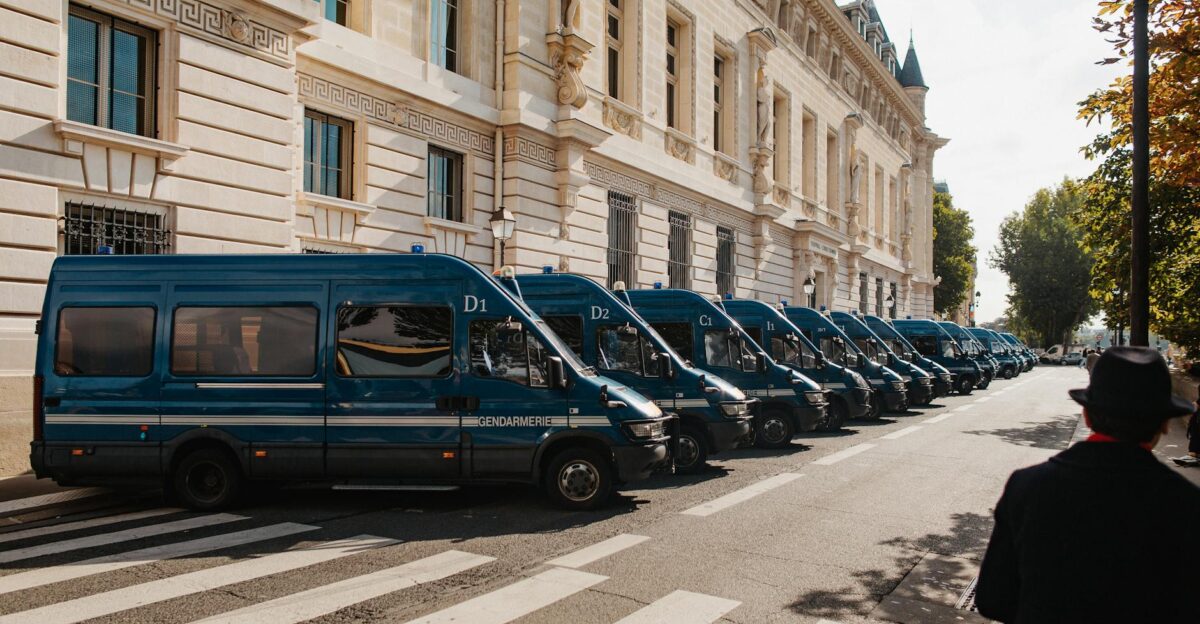 Line of blue police vans parked on a city street beside a historical building