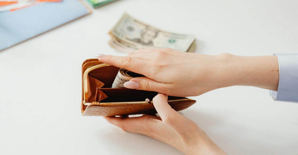 Close-up of hands placing cash into a leather wallet with bills on table